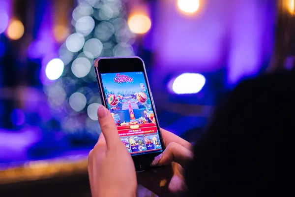 4777BED App — Enjoy seamless gaming on your smartphone A young woman relaxing with her phone while dynamic casino elements float around her, illustrating the smooth mobile experience offered by the 4777BED app.